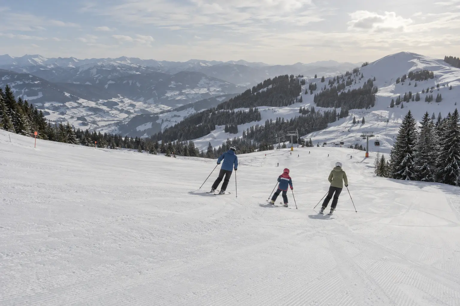 Familie fährt auf einer breiten Skipiste talwärts