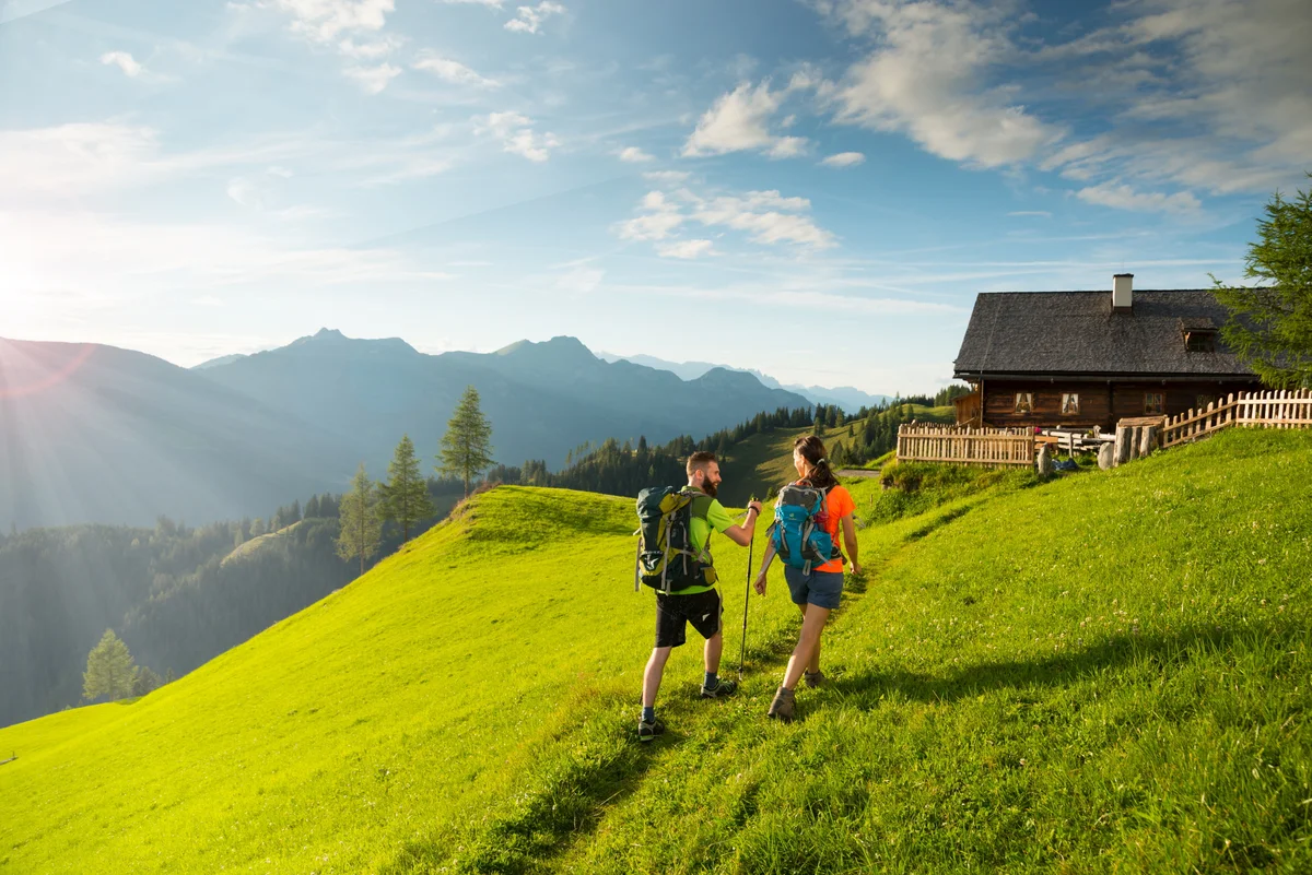 Zwei Wanderer auf dem Weg zur Bichlalm im sommerlichen Großarltal, im Hintergrund die Almhütte